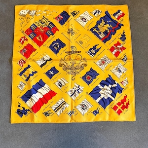 May include: A square yellow silk scarf featuring a central anchor emblem and a variety of historical maritime flags arranged in a grid pattern. Each flag is labeled with text, including Royal d'Angleterre and De la République de Venise.
