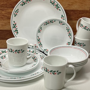 Puede incluir: Un juego de vajilla blanco con un diseño de acebo. El juego incluye platos, cuencos y tazas. Los platos y cuencos tienen un borde verde con acentos de acebo. Las tazas tienen una banda de acebo. Ideal para reuniones festivas.