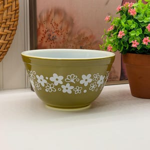 Peut inclure: Un bol mélangeur vert olive avec un intérieur blanc et un motif répétitif de fleurs blanches sur l'extérieur. Le bol présente une forme arrondie et lisse avec un bord large et une base effilée, orné de diverses formes florales.