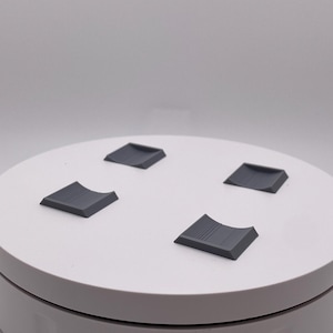 May include: A white turntable with four gray rubber feet. The turntable is designed to rotate objects for photography or video.