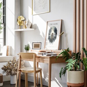 Op de afbeelding: Een thuiskantoorwerkplek met een houten bureau en stoel, een potplant en een ingelijst afdruk met de tekst "The Mask".