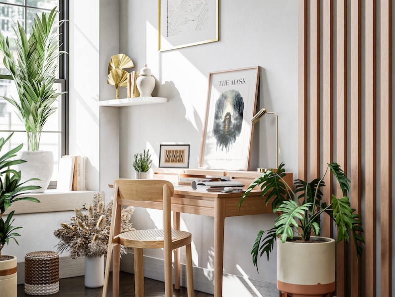 Op de afbeelding: Een thuiskantoorwerkplek met een houten bureau en stoel, een potplant en een ingelijst afdruk met de tekst "The Mask".