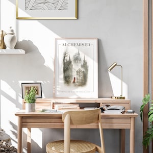 K&ouml;nnte beinhalten: Ein heller Holzschreibtisch mit einem gerahmten Druck mit der Aufschrift "ALCHEMISED" und einer Zeichnung eines Schlosses. Eine kleine Schreibtischlampe und eine Topfpflanze stehen auf dem Schreibtisch. Ein Holzstuhl steht vor dem Schreibtisch.