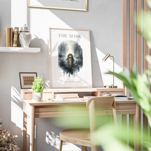 Op de afbeelding: Een ingelijste poster met de titel "THE MASK" en de tekst "FALL UPON THE LAND" in een lichtgrijs frame op een witte muur. De poster toont een aquarel illustratie van een vrouw met een masker in een bosomgeving.