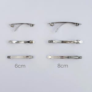 Puede incluir: Varias horquillas de metal plateado, mostrando diferentes diseños. La imagen incluye estilos curvos y rectos. Los tamaños se indican como 6 cm y 8 cm. Estos accesorios para el cabello son adecuados para varios peinados.