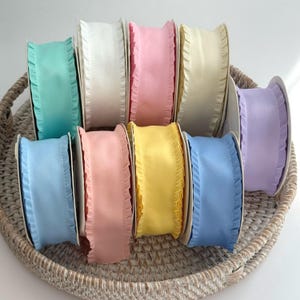 May include: A collection of colorful satin ribbons with ruffled edges. The spools display shades of blue, pink, yellow, white, and lavender. The ribbons are arranged in a woven basket, perfect for crafting and gift wrapping.