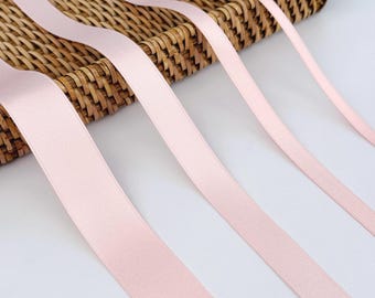 May include: Several strands of pale pink satin ribbon are arranged diagonally across a woven basket. The ribbons have a smooth, glossy texture and are of varying widths. The background is a light, neutral color, providing contrast to the ribbons.