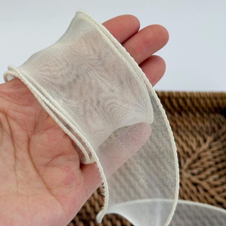 May include: Off-white sheer ribbon with a delicate, woven texture. The ribbon has a subtle sheen and is edged with a thin, cream-colored trim. This decorative ribbon is suitable for crafts, gift wrapping, and various DIY projects.