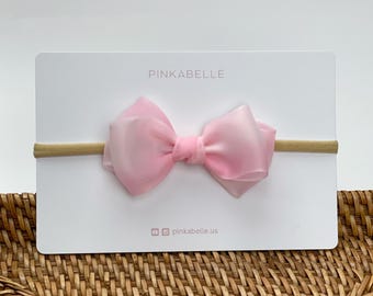 May include: A pink satin bow headband on a white card with the text "PINKABELLE" and "pinkabelle.us".