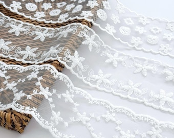 May include: Three strips of white lace trim featuring distinct embroidered floral and geometric patterns. Each strip is made of sheer mesh fabric with scalloped edges, showcasing intricate white thread work in various repeating designs.