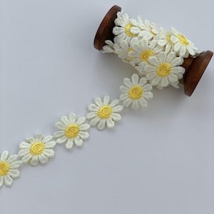 May include: White daisy trim with yellow centres, wound around a wooden spool.