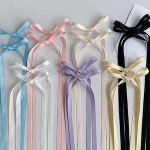 May include: A collection of hair ribbons in various pastel colors, including light blue, pink, white, lavender, and cream. Each ribbon features a delicate bow at the top and long, flowing streamers.
