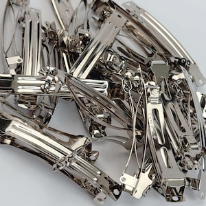 May include: A collection of silver-toned metal hair barrettes with a polished finish. Each hair clip features a spring-loaded mechanism and a hinged clasp. The metal components are arranged in a pile, showing the structural design of the clips.