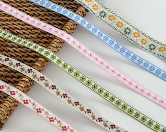 May include: Assortment of floral ribbon in various colors, including green, pink, blue, and cream. Each ribbon features a repeating pattern of small flowers. The ribbons are arranged diagonally, showcasing their different designs and colors.