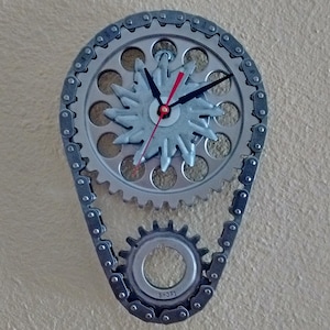 May include: A silver clock with a chain and gears. The clock face is a starburst design with black hands and red second hand. The chain is labeled "1301-S".