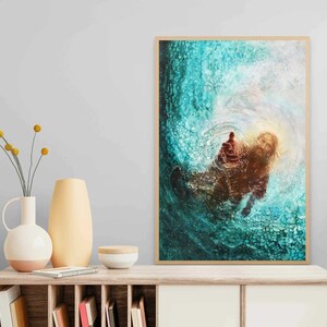 K&ouml;nnte beinhalten: Ein gerahmtes Kunstwerk, das eine Figur zeigt, die aus wirbelndem t&uuml;rkisfarbenem Wasser eine Hand ausstreckt. Das Kunstwerk hat einen warmen, goldenen Schein, der mit den k&uuml;hlen T&ouml;nen des Wassers kontrastiert. Das Kunstwerk wird auf einem Holzschrank ausgestellt.