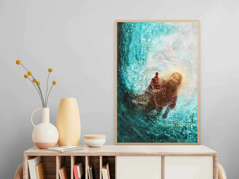 K&ouml;nnte beinhalten: Ein gerahmtes Kunstwerk, das eine Figur zeigt, die aus wirbelndem t&uuml;rkisfarbenem Wasser eine Hand ausstreckt. Das Kunstwerk hat einen warmen, goldenen Schein, der mit den k&uuml;hlen T&ouml;nen des Wassers kontrastiert. Das Kunstwerk wird auf einem Holzschrank ausgestellt.