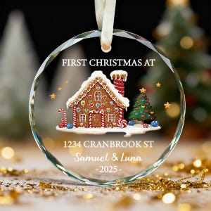 K&ouml;nnte beinhalten: Ein klarer, runder Weihnachtsschmuck mit einem Lebkuchenhaus-Design. Der Schmuck tr&auml;gt den Text "FIRST CHRISTMAS AT" oben, die Adresse "1234 CRANBROOK ST", die Namen "Samuel & Luna" und das Jahr "-2025-".