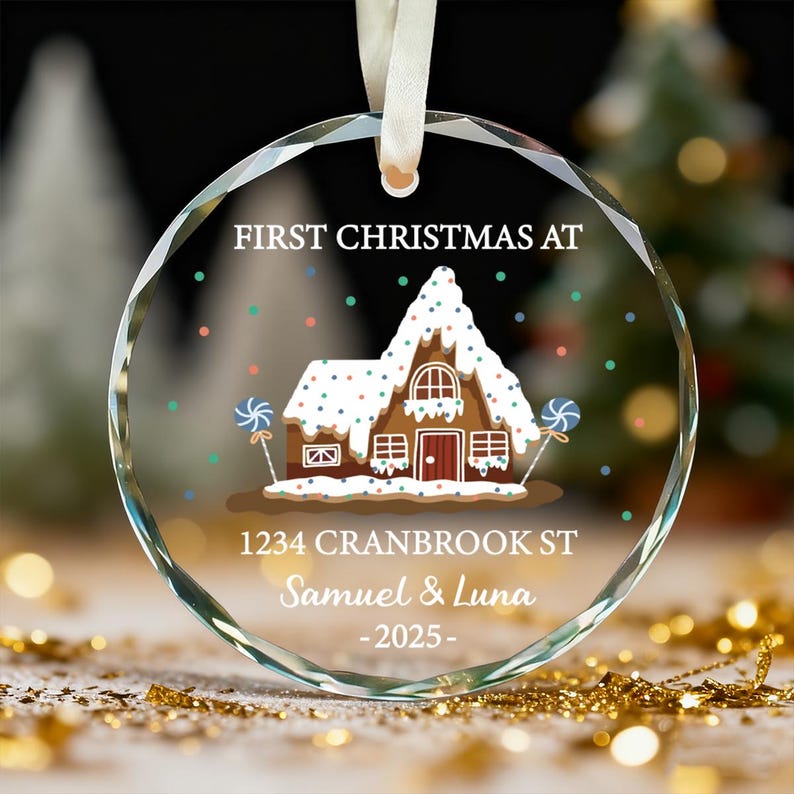 K&ouml;nnte beinhalten: Ein klarer, runder Weihnachtsschmuck mit einer Lebkuchenhaus-Illustration. Der Text "FIRST CHRISTMAS AT" und die Adresse sind sichtbar. Der Schmuck wird von einem wei&szlig;en Band gehalten und enth&auml;lt den Text "Samuel & Luna -2025-".
