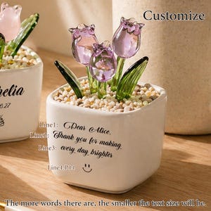 Op de afbeelding: Een kleine witte keramische pot met drie glazen tulpenbloemen in paars en groen. De pot bevat kleine kiezels en heeft de tekst "Dear Alice, Thank you for making every day brighter" en een smiley.