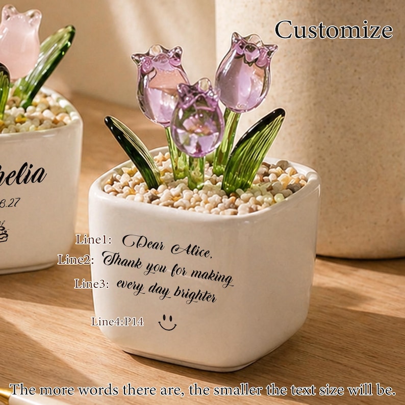 Op de afbeelding: Een kleine witte keramische pot met drie glazen tulpenbloemen in paars en groen. De pot bevat kleine kiezels en heeft de tekst "Dear Alice, Thank you for making every day brighter" en een smiley.