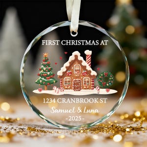 K&ouml;nnte beinhalten: Ein klarer, runder Weihnachtsschmuck mit festlichem Design. Der Schmuck zeigt ein Lebkuchenhaus, einen Weihnachtsbaum und den Text "FIRST CHRISTMAS AT" und "1234 CRANBROOK ST Samuel & Luna -2025-".