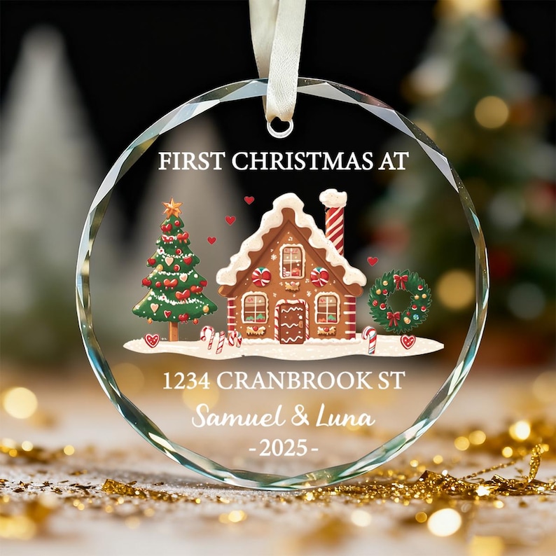 K&ouml;nnte beinhalten: Ein klarer, runder Weihnachtsschmuck mit festlichem Design. Der Schmuck zeigt ein Lebkuchenhaus, einen Weihnachtsbaum und den Text "FIRST CHRISTMAS AT" und "1234 CRANBROOK ST Samuel & Luna -2025-".