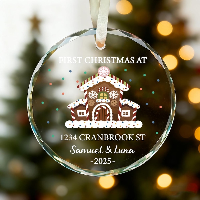 K&ouml;nnte beinhalten: Ein klarer, runder Weihnachtsschmuck mit einem Lebkuchenhaus-Design. Der Schmuck tr&auml;gt den Text "FIRST CHRISTMAS AT" &uuml;ber dem Haus und darunter "1234 Cranbrook St Samuel & Luna -2025-". Ein wei&szlig;es Band ist zum Aufh&auml;ngen befestigt.