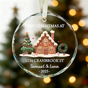 K&ouml;nnte beinhalten: Ein klarer, facettierter Weihnachtsbaumschmuck aus Glas mit einem festlichen Lebkuchenhaus- und Weihnachtsbaumdesign. Der Schmuck enth&auml;lt den Text "FIRST CHRISTMAS AT", Adresse, Namen und das Jahr 2025. Ein wei&szlig;es Band ist zum Aufh&auml;ngen befestigt.
