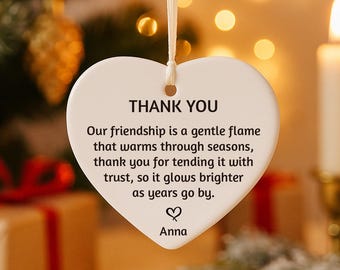 May include: A white heart-shaped ornament with the words "THANK YOU" in black. The ornament has a cream-colored ribbon for hanging and a message about friendship. The name "Anna" is at the bottom.