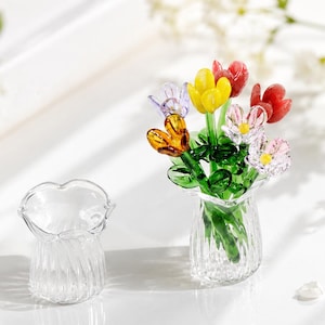 May include: A clear glass vase with a fluted design and a bouquet of miniature glass flowers in yellow, red, orange, purple, and pink with green stems and leaves. An identical empty clear glass vase sits beside the flower arrangement.