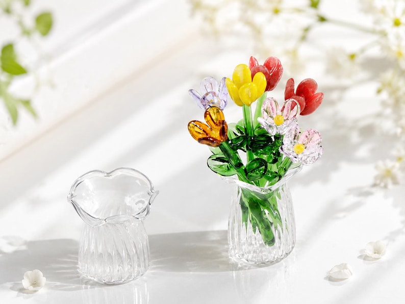 May include: A clear glass vase with a fluted design and a bouquet of miniature glass flowers in yellow, red, orange, purple, and pink with green stems and leaves. An identical empty clear glass vase sits beside the flower arrangement.