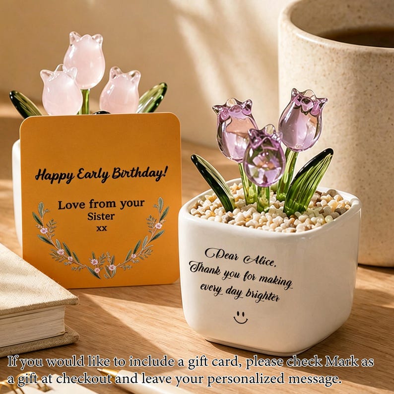 Op de afbeelding: Een decoratief glazen tulpenarrangement in een witte vierkante pot met kleine steentjes. Het arrangement bevat drie paarse tulpen en groene bladeren. Een kaart leest "Happy Early Birthday! Love from your Sister".