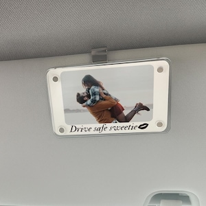 May include: A clear acrylic car visor clip with a photo of a couple embracing. The photo is framed with a white border and the text "Drive safe sweetie" is printed below the image, along with a lip print.
