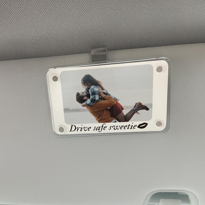 May include: A clear acrylic car visor clip with a photo of a couple embracing. The photo is framed with a white border and the text "Drive safe sweetie" is printed below the image, along with a lip print.
