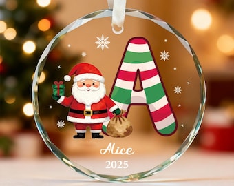 May include: A clear, round Christmas ornament with a Santa Claus illustration and the letter "A" in red, green, and white stripes. The ornament has the name "Alice" and the year "2025" printed on it. A white ribbon is attached for hanging.