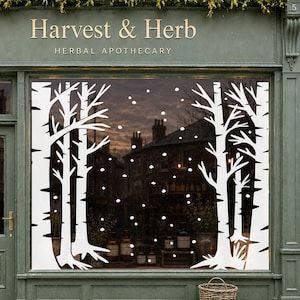 May include: A storefront window display for Harvest & Herb Herbal Apothecary featuring white vinyl decals of bare trees and falling snow. The design covers the glass, framing the interior view of the shop with a winter forest theme.