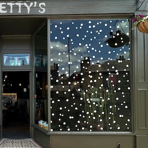 Könnte beinhalten: Geschäftseingang mit der Aufschrift "ETTY'S" über dem Eingang. Im Schaufenster spiegelt sich ein blauer Himmel mit weißen Punkten. Ein hängender Korb mit Blumen und Grün ist zu sehen.