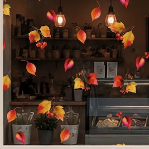 Könnte beinhalten: Ein Fensteraufkleber-Set mit verstreuten Herbstblättern in Gelb-, Orange- und Rottönen, durchsetzt mit kleinen roten Beerenclustern. Das Design umfasst einzelne Blätter und kleine Zweige, die eine saisonale Dekoration bilden.