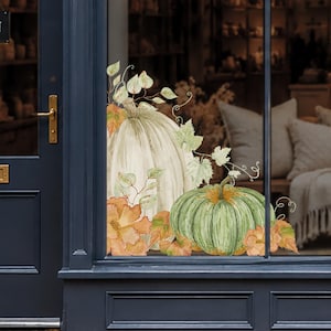 Peut inclure: Un autocollant pour fenêtre représentant une grande citrouille crème pâle et une citrouille verte côtelée plus petite. Le motif comprend des feuilles d'automne orange et jaunes, du feuillage vert et des vrilles délicates en aquarelle.