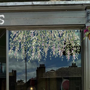Può includere: Una vetrina decorata con un motivo floreale di glicine. Il design presenta foglie verdi e fiori viola che pendono su uno sfondo blu scuro, con riflessi di edifici.