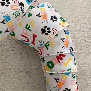 May include: White ribbon printed with colourful text and paw prints. The ribbon features the words "MEOW", "WOOF", "PURR", and "RUFF" in various colours, along with bone and fish graphics. The edges are finished with a white stitched trim.
