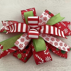 May include: A festive Christmas bow featuring red and white striped ribbon, green ribbon, and red ribbon with candy cane and peppermint patterns. The bow is a decorative accent for holiday decor.