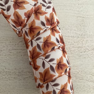 May include: A roll of white ribbon with a brown and orange leaf pattern and a copper-colored edge.