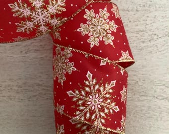 Puede incluir: Cinta roja con un patrón repetido de copos de nieve blancos y dorados. La cinta tiene un borde dorado y está enrollada, mostrando el diseño. Esta cinta festiva es adecuada para decoraciones navideñas y manualidades.