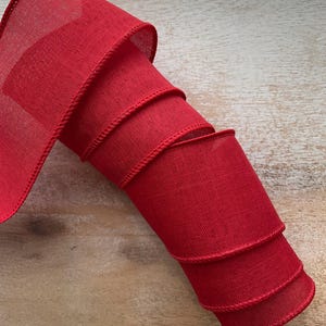 May include: Red wired ribbon with a textured finish. The ribbon is rolled up and ready to be used for crafting or decorating.