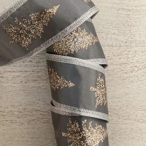 May include: A roll of grey ribbon with silver trim and gold glitter Christmas tree designs. The ribbon is tightly coiled, showcasing the festive pattern. Suitable for holiday crafts and gift wrapping.