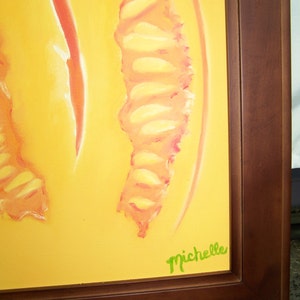 May include: A yellow canvas painting with a pink and yellow abstract design. The painting is framed in a dark brown wood frame. The artist's signature, "Michelle", is written in green paint in the bottom right corner.