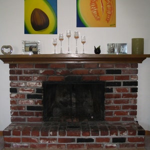 May include: A brick fireplace with a black metal fire screen. Above the fireplace are two framed paintings, one of a cantaloupe and one of an avocado. There are also four clear glass candle holders on the mantel.