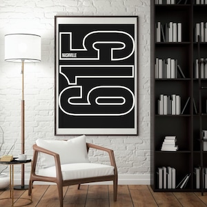 May include: A framed black and white art print with the numbers "615" in a bold, outlined font. The word "Nashville" is above the numbers. The print is displayed on a white brick wall.